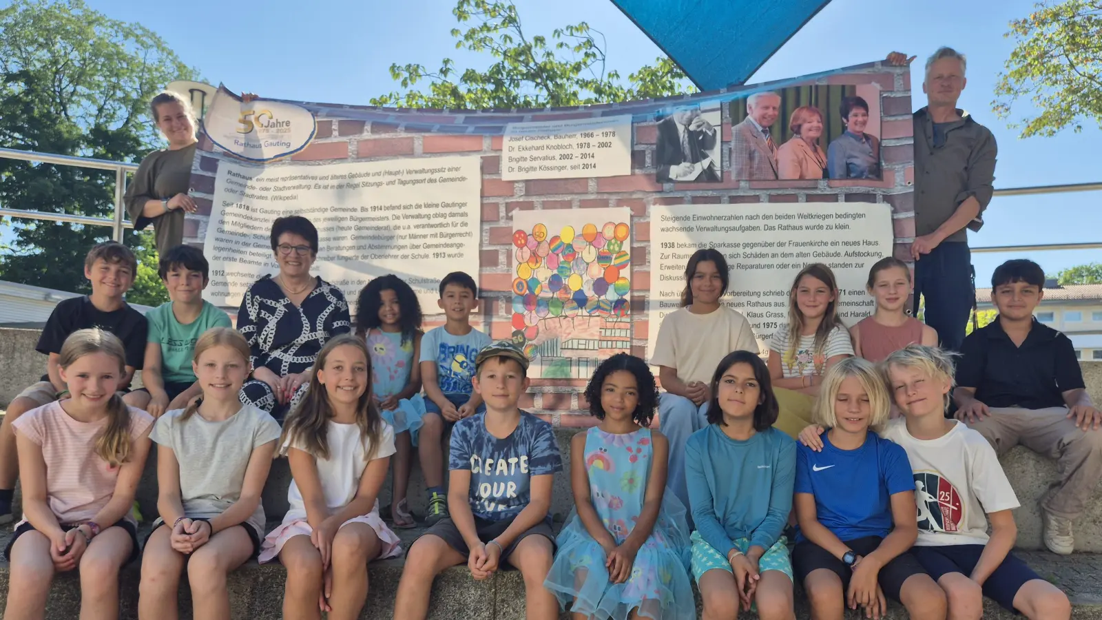 Spaß mit Banner (1. Reihe v.l.): Franziska, Clara, Karla, Anton, Kaya, Mara, Simon und Tom, (2. Reihe v.l.) Bene, Ben Luca, Brigitte Kössinger, Zoë, Vicenzo, Milana, Karlotta, Josefine und Muhammed sowie (dahinter mit Banner) Klassenlehrerin Isabella Roman und Rathausmitarbeiter Sebastian Hofmüller. (Foto: Gemeinde Gauting)
