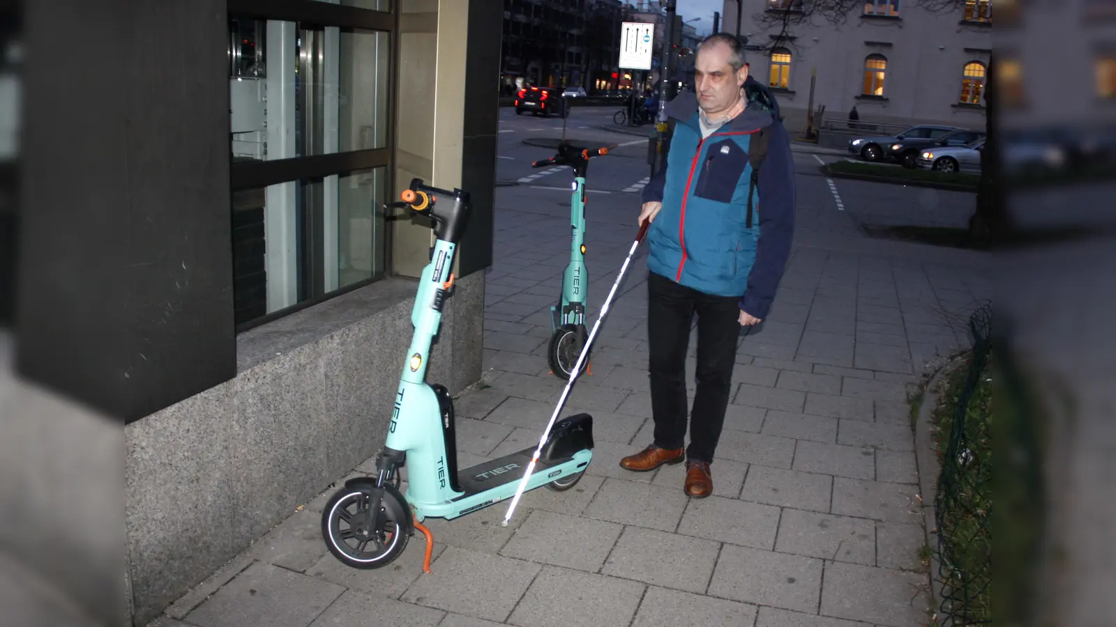 Am Laimer Platz erklärt Stefan Unterstraßer, warum auf dem Gehweg zurückgelassene Roller für ihn gefährliche Stolperfallen sind. Zudem machen es ihm die Scooter wie hier unmöglich, sich mit seinem Taststock an der Kante entlang des U-Bahn-Aufzugs und des Gehweg zu orientieren. (Foto: job)