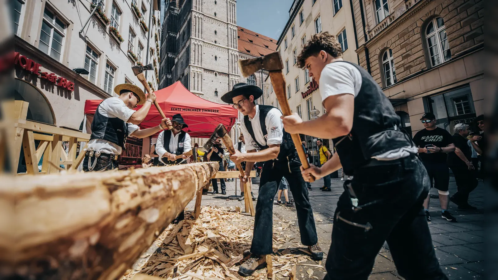 Mitarbeiter einer Zimmerei behauen Eichenbalken beim Bennofest. Aus ihnen entsteht ein Arma-Kreuz für die Kirche St. Barbara in Schwabing-West.  (Foto: Frank Zimmerei und Holzbau )