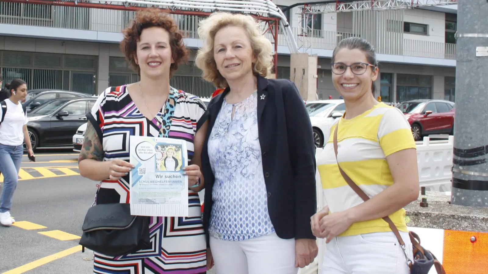 Magdalena Pentek (Elternbeirat), Schulleiterin Monika Engelmayer und Karlla Soares (von links) hoffen auf Schulweghelfer, die den Kindern sicher über die große Kreuzung vor der neuen Schule (hinten) helfen. (Foto: job)